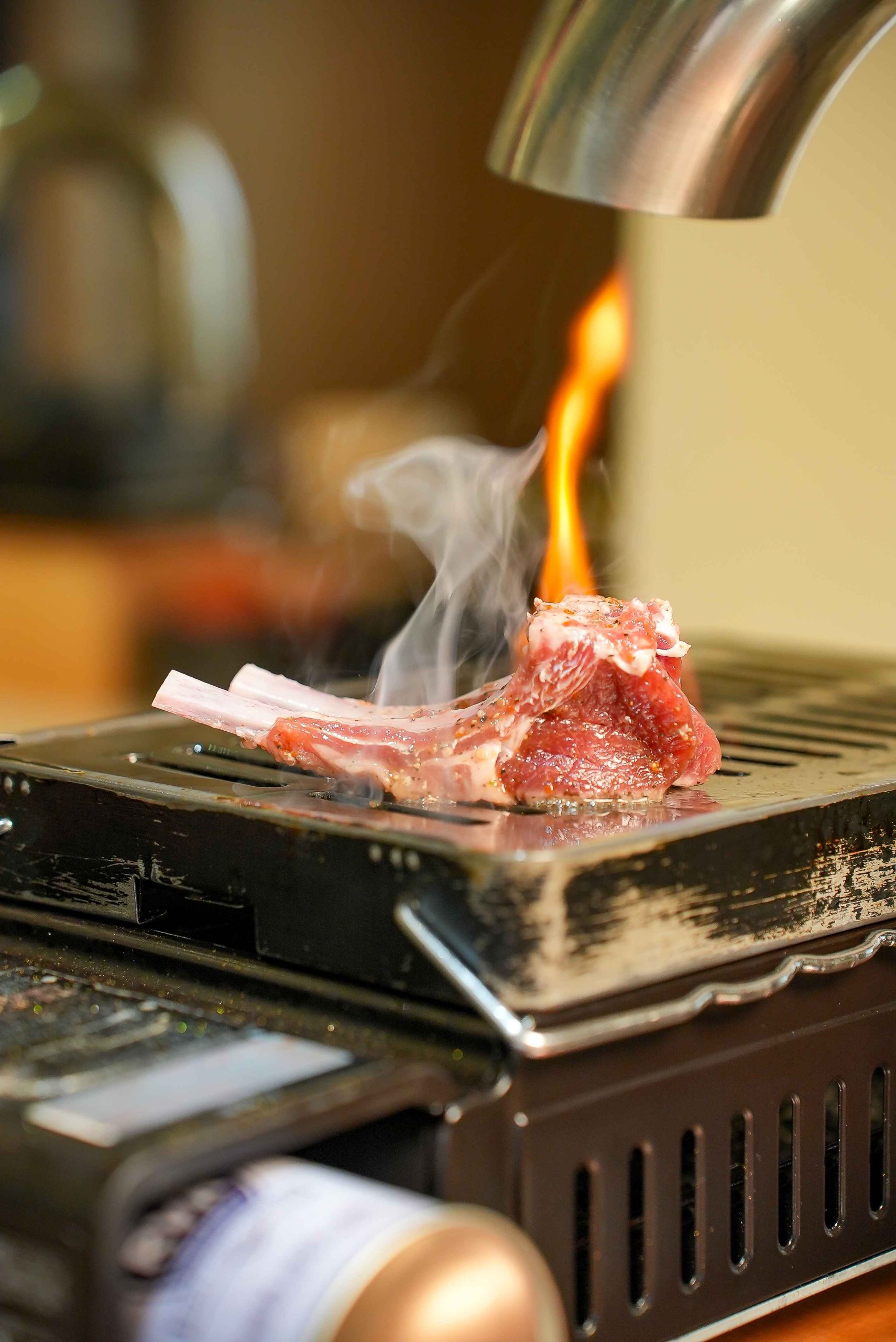 A rack of Lumina lamb searing over open flame on the tabletop grill at KOBU